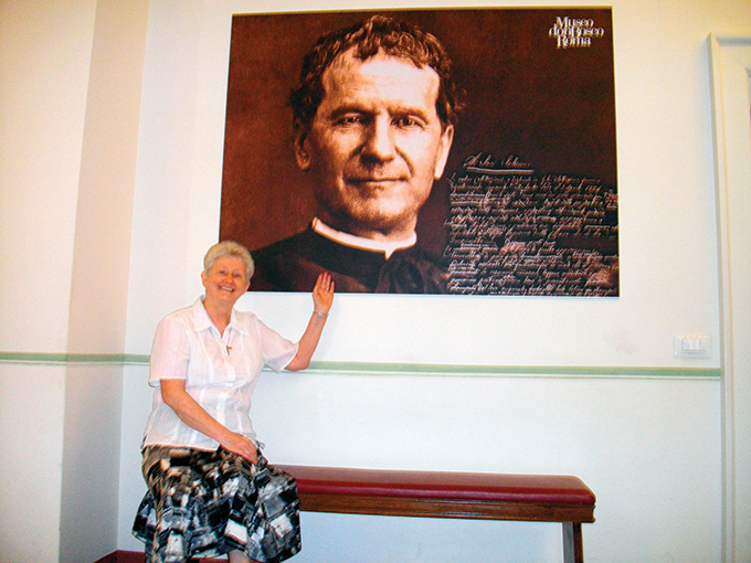 Assise sous une affiche illustrant Don Bosco, Sr Suzanne Allard salue les Amis du père Prévost